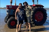 two men stand on the beach next to a tractor