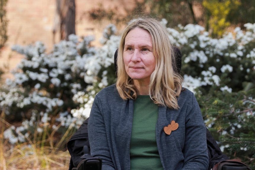 A woman sits in a wheelchair in front of flowers.