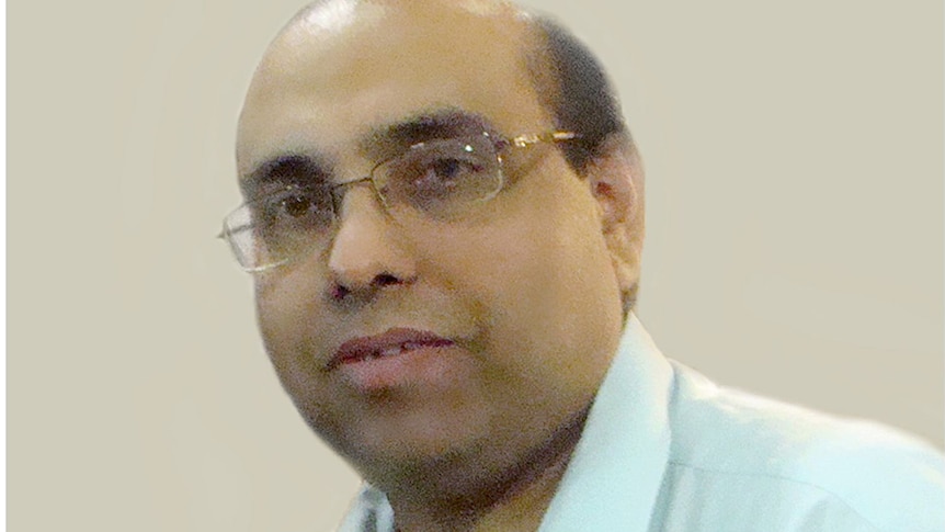 An Indian man with glasses wearing a light white shirt looking at the camera