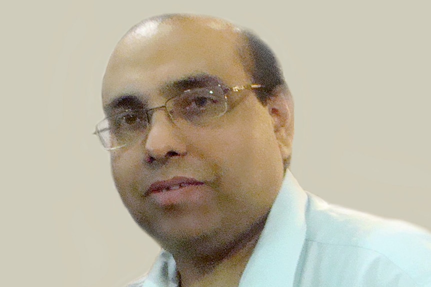 An Indian man with glasses wearing a light white shirt looking at the camera