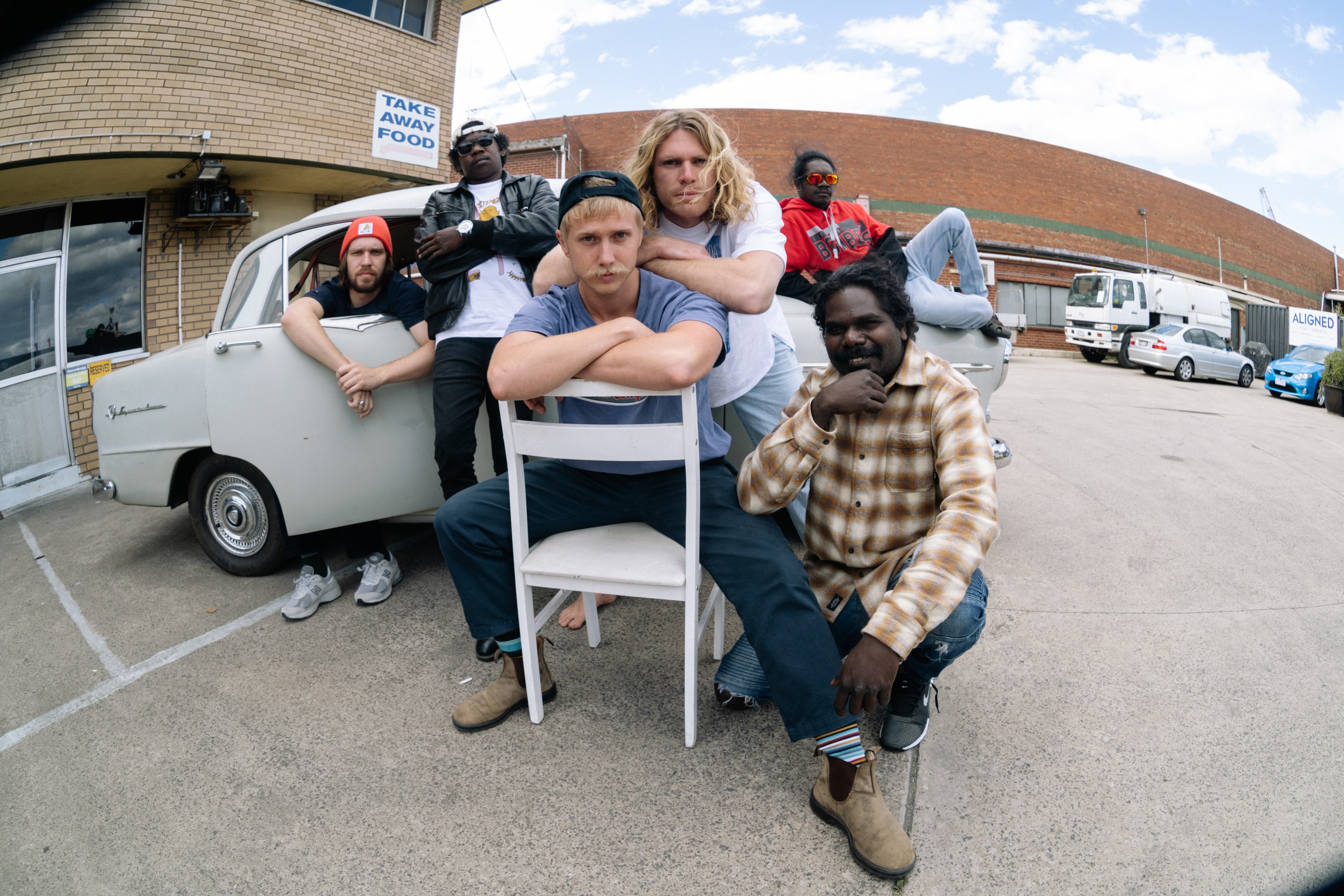 The members of King Stingray pose in and around a parked car in a car park outside 