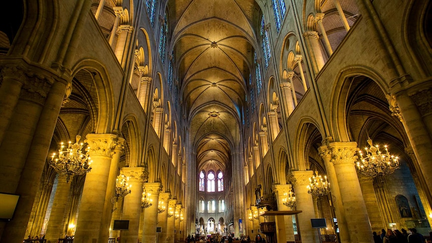 Candles illuminate pews, domes and archways of Notre Dame Cathedral as people mill about in the distance