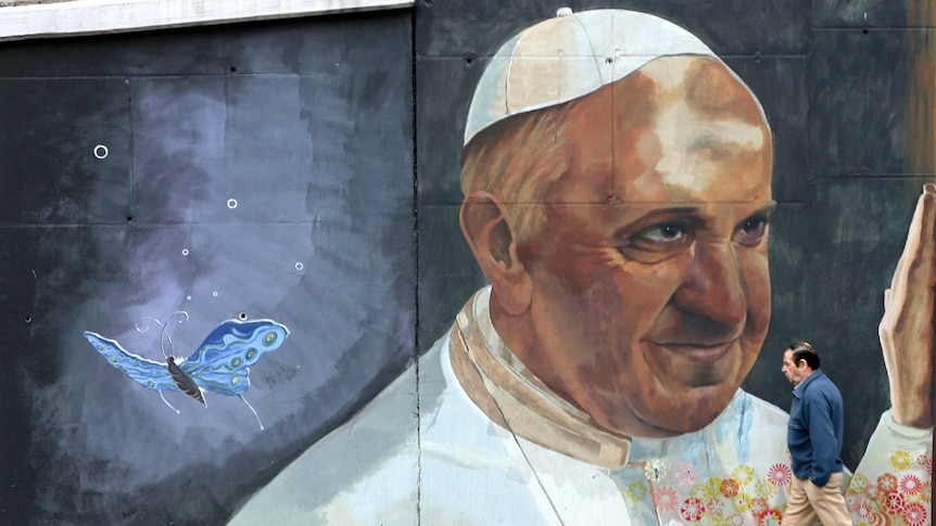 A man walks in front a large painted mural featuring Pope Francis in Buenos Aires, Argentina.