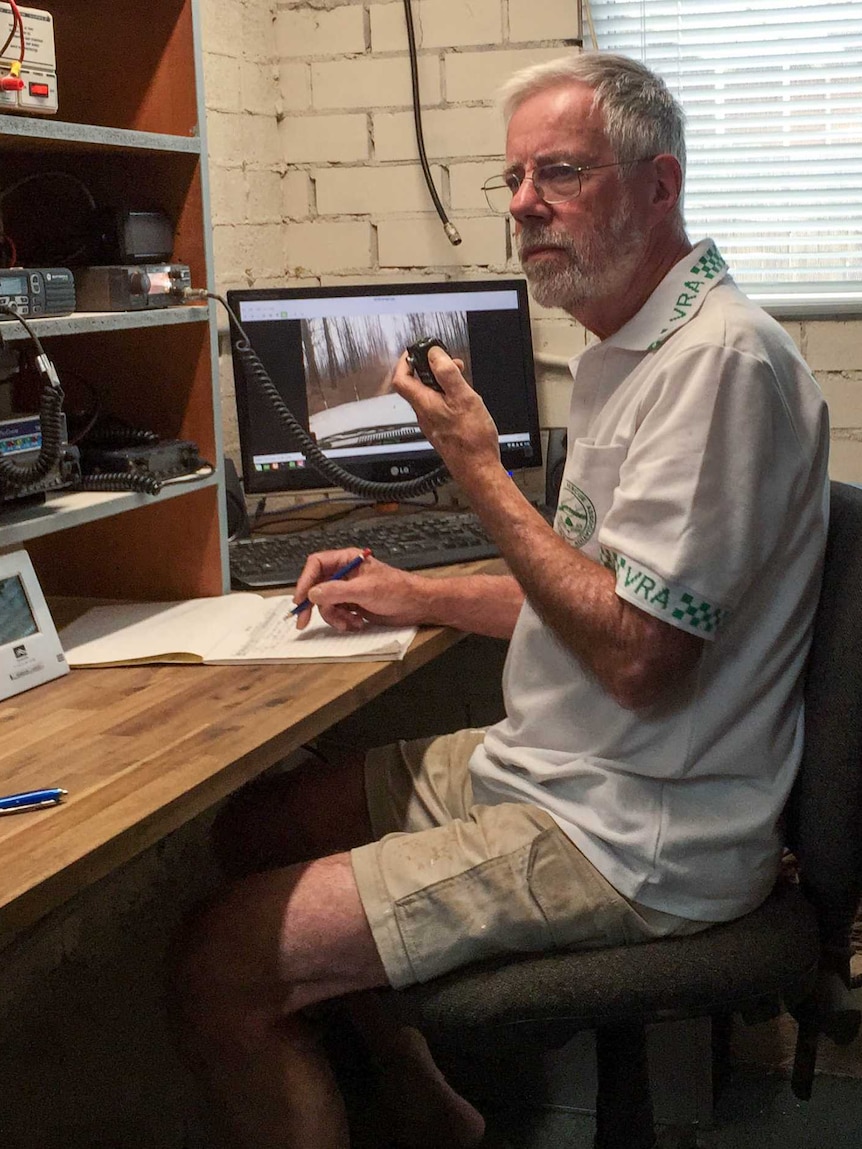 A man sits at a desk operating a radio