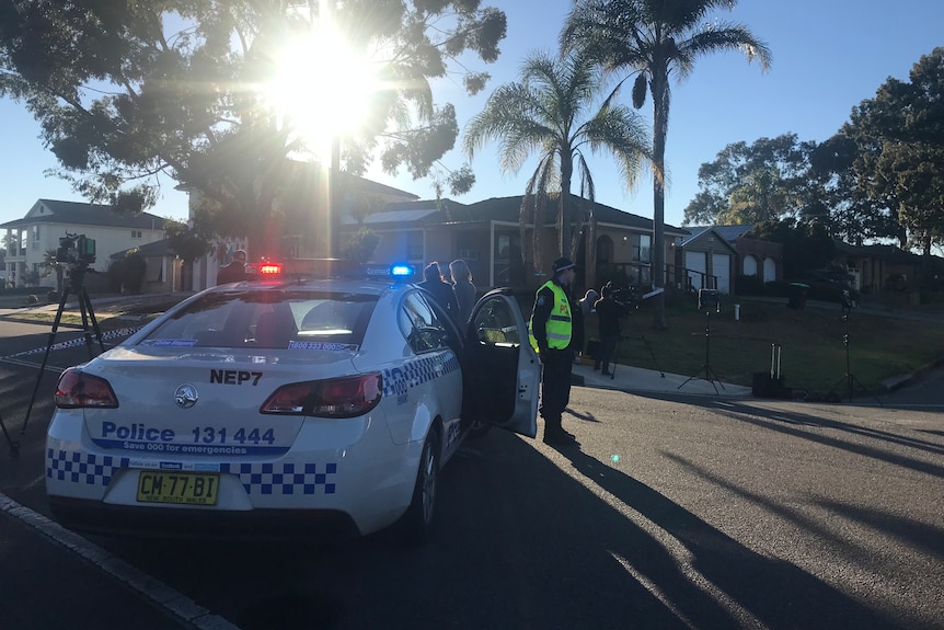 A policeman stands by his patrol car in a taped-off street near a crime scene