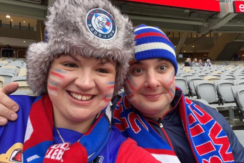 Two Western Bulldogs AFL supporters, a woman and man, wearing club colours at a game.  