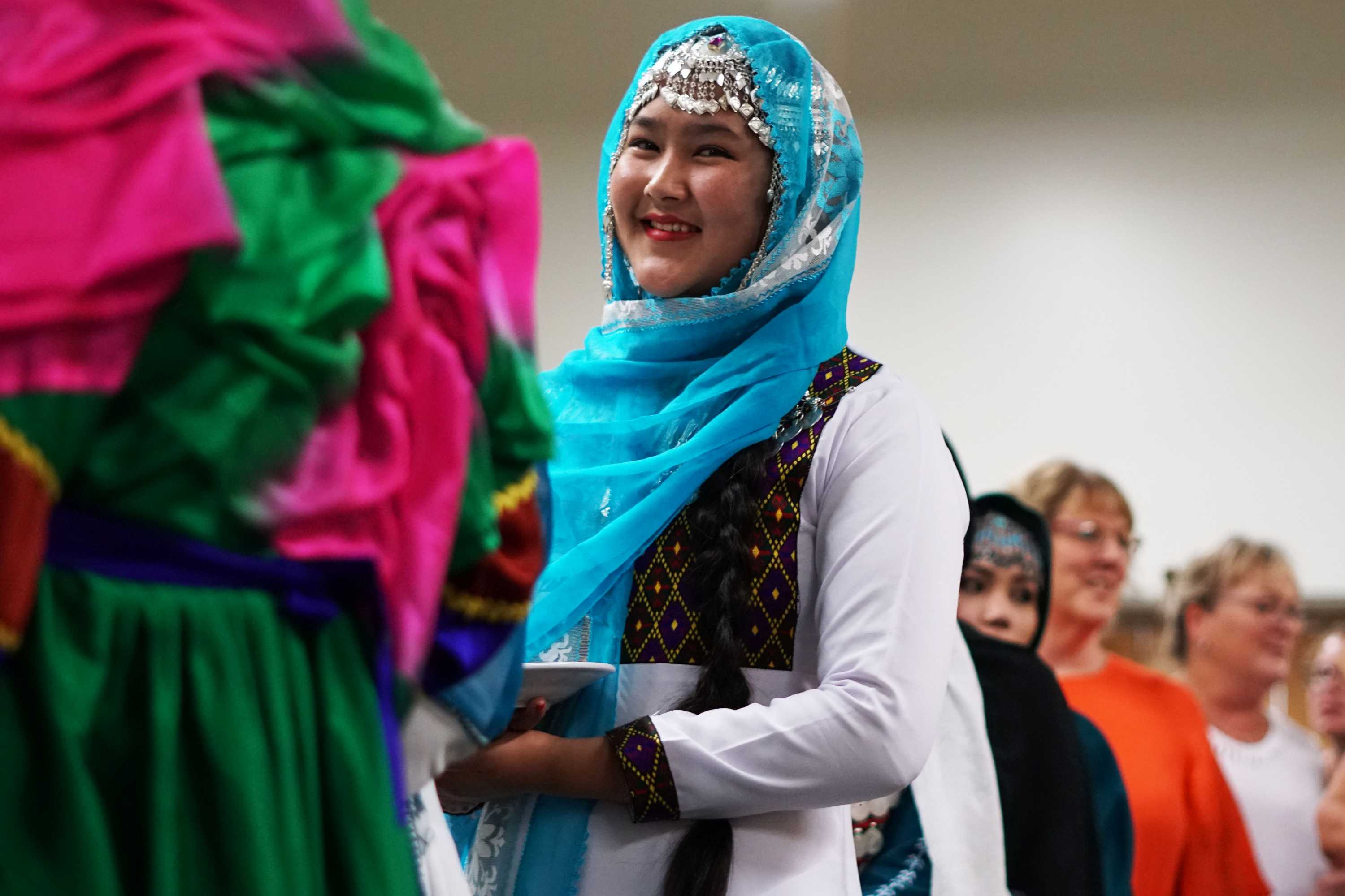 A girl stands in line for food smiling, wearing traditional dress.