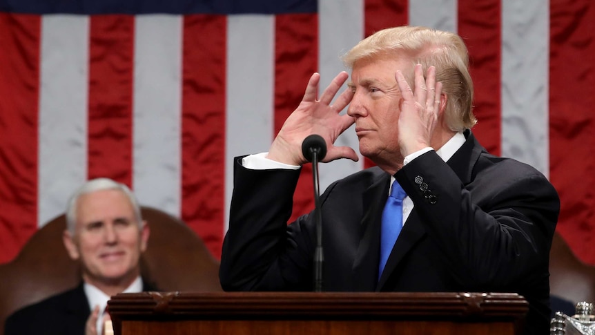 US Vice-President Mike Pence watches as President Donald Trump holds his hands to his head while standing in front of a US flag.