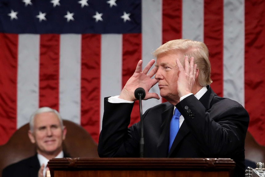 US Vice President Mike Pence watches as President Donald Trump holds his hands to his head while standing in front of a US flag.