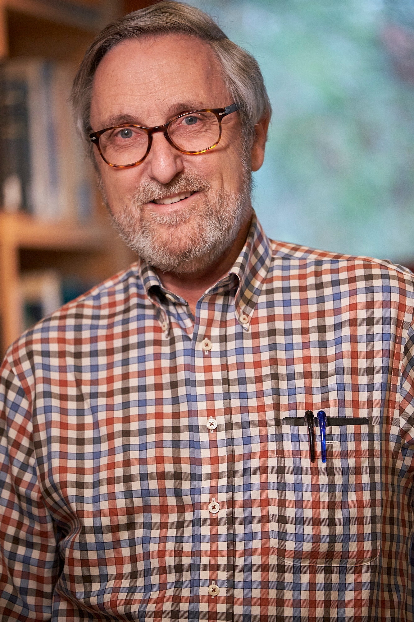 Un hombre mayor con gafas y camisa a cuadros sonríe.