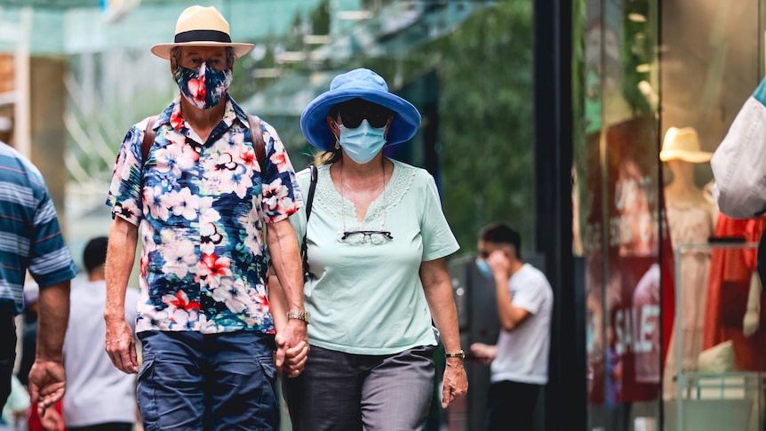 a man and a woman holding hands and wearing face masks