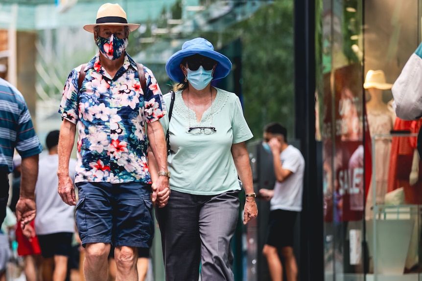 a man and a woman holding hands and wearing face masks