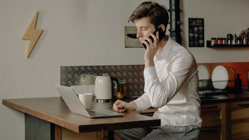 A man in a business shirt and short sits at a laptop.