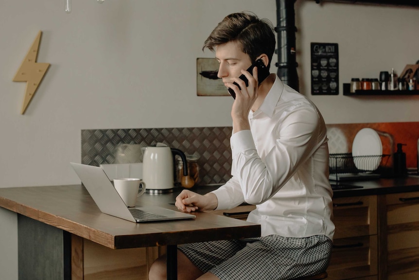 A man in a business shirt and short sits at a laptop.