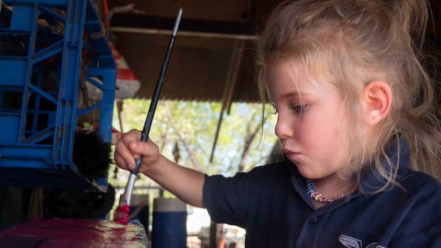 A girl holds a paintbrush.