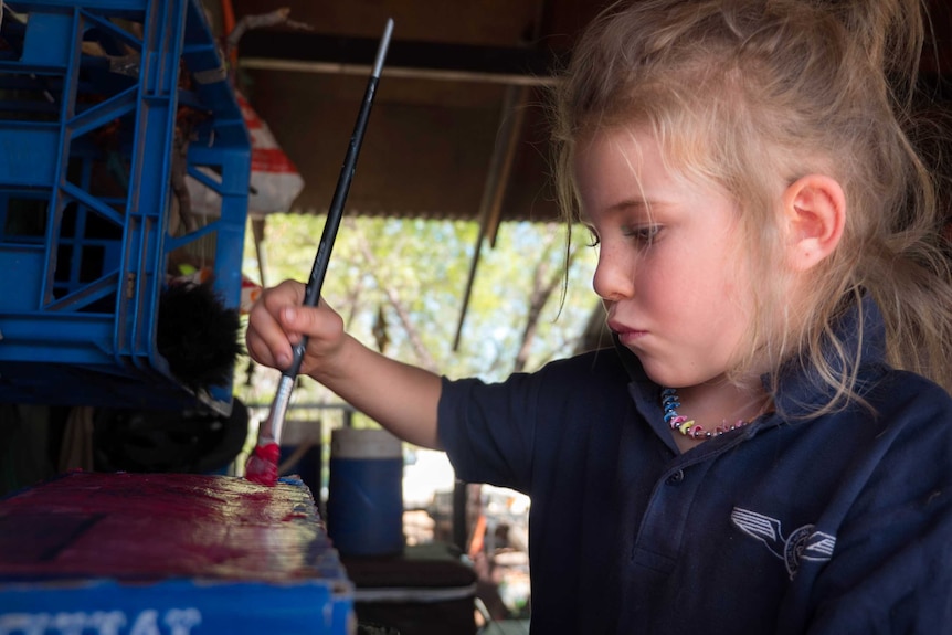 A girl holds a paintbrush.