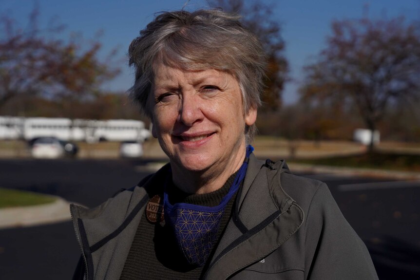 A woman with grey hair and wearing an I voted badge smiles as she stares at the camera.