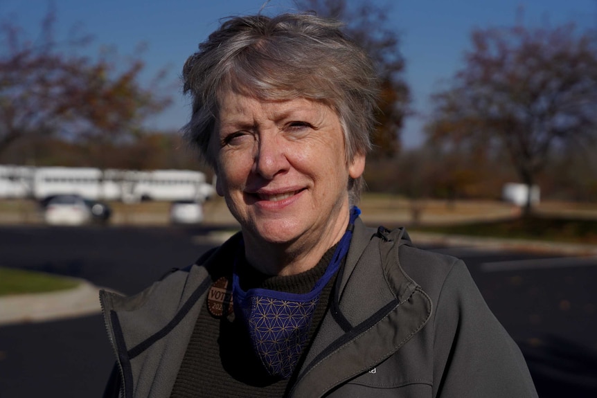 A woman with grey hair and wearing an I voted badge smiles as she stares at the camera.