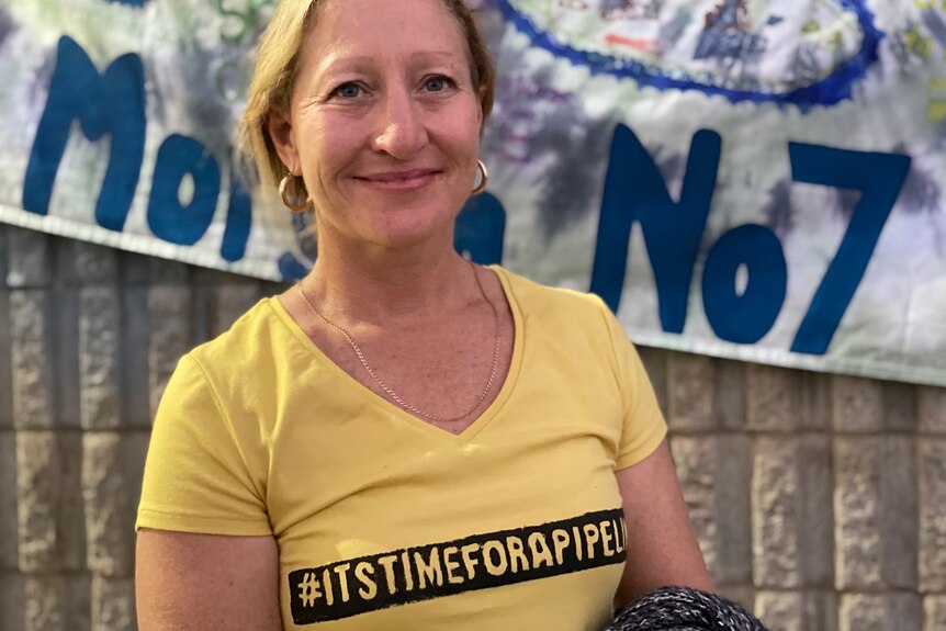 Kirra Swain sonríe a la cámara, vistiendo una camiseta amarilla con las palabras #itstimeforapipeline.