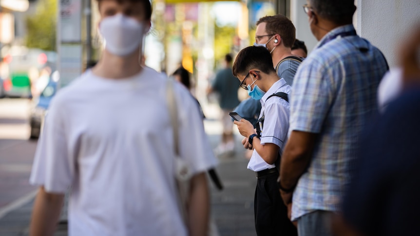 People lined up next to a bus sign with masks on.