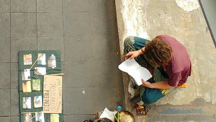 An aerial photo shows a dread-locked begger selling postcards and with a gong.