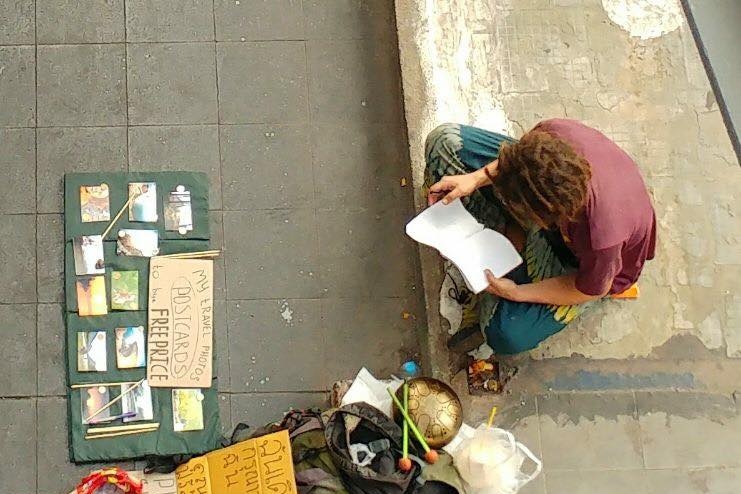 An aerial photo shows a dread-locked begger selling postcards and with a gong.