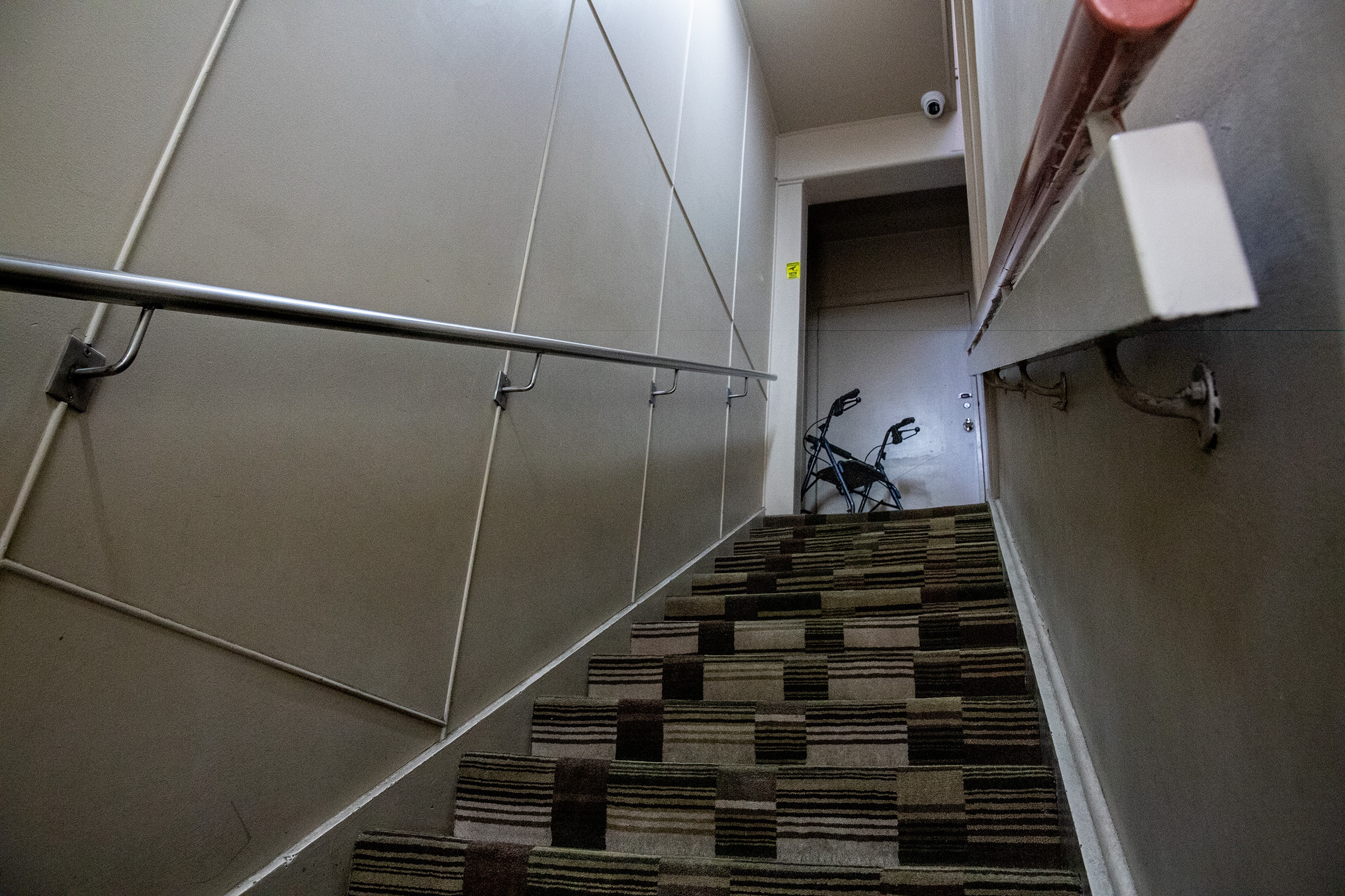 View looking up a steep stair case covered in brown and white check pattern. A walker sits at the top of the stairs.