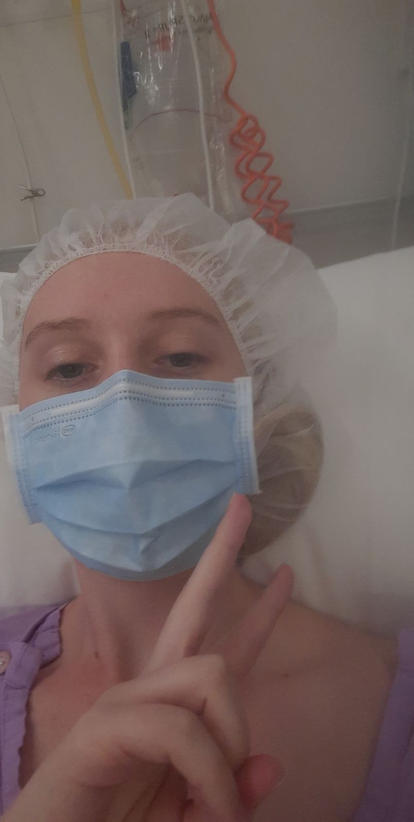 a young women in a cap and mask waitnng for surgery lying down 