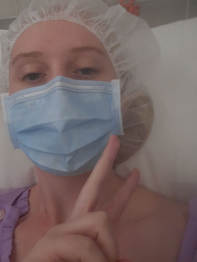 a young women in a cap and mask waitnng for surgery lying down 