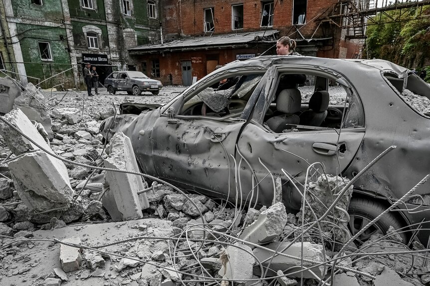 Une femme se tient près de sa voiture détruite près d'un ancien moulin après une frappe de missile.