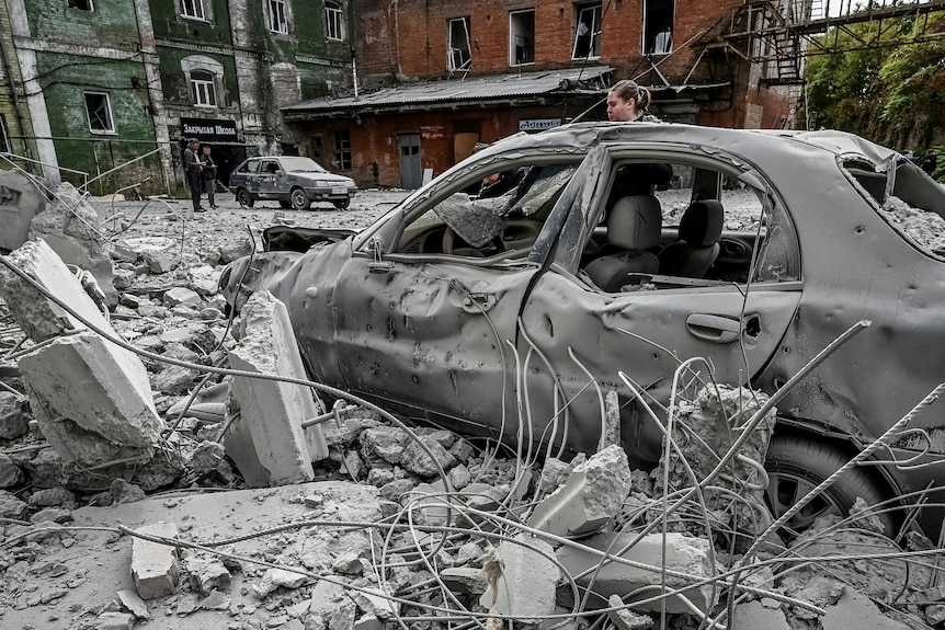 在导弹袭击后，一名妇女站在她被毁坏的汽车附近，靠近一座旧磨坊。