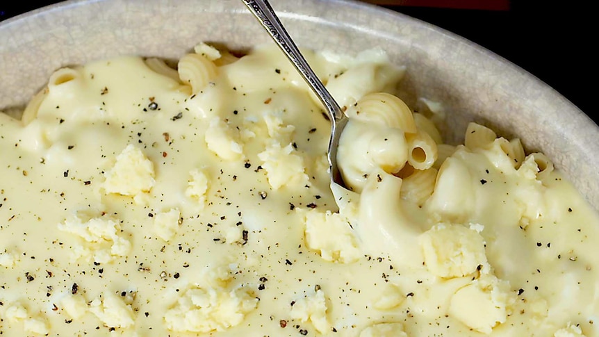 Close up photo of mac and cheese in a bowl with cracked pepper and extra cheese.