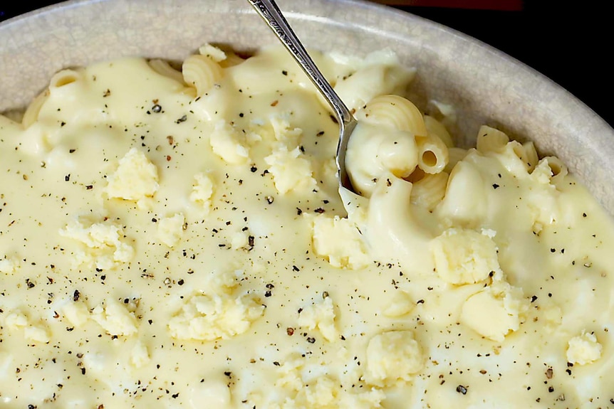 Close up photo of mac and cheese in a bowl with cracked pepper and extra cheese.