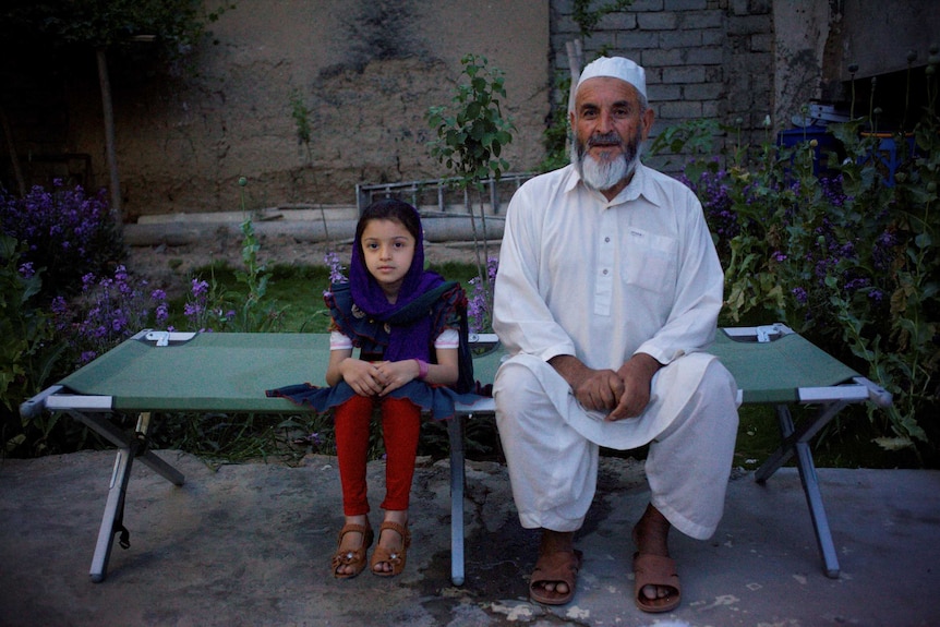 A man sits with his granddaughter on a military cot bed in his hospital garden in Helmand.