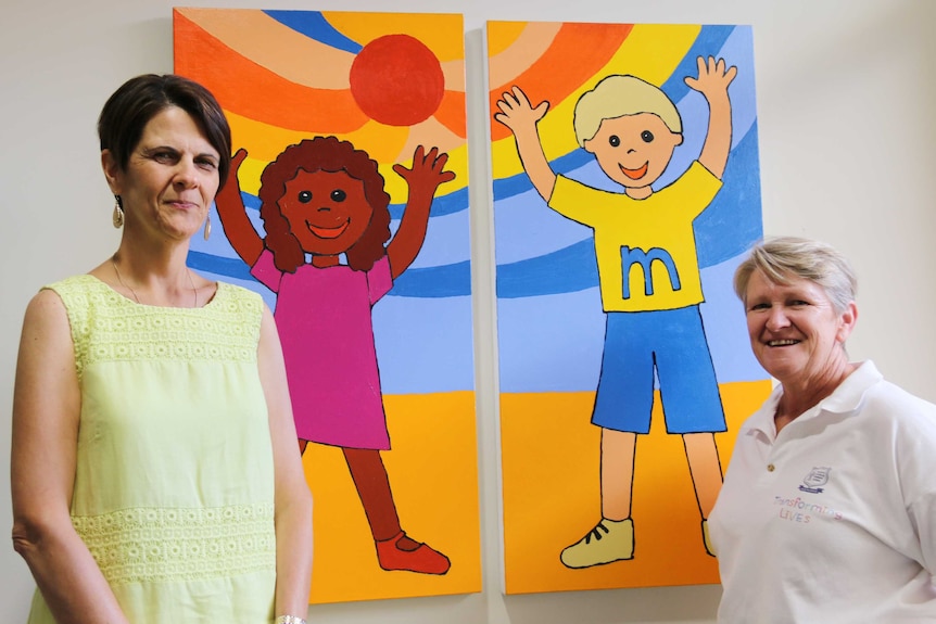 Lina Bertolini and Jo Boyd pose for the camera in front of a bright painting of two children.