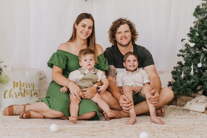 A young woman and man with two kids sitting in their laps beside a christmas tree. 