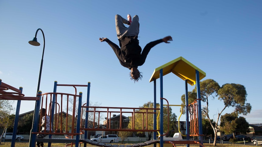 Mohamed's friend does a backflip off the suburban play ground.