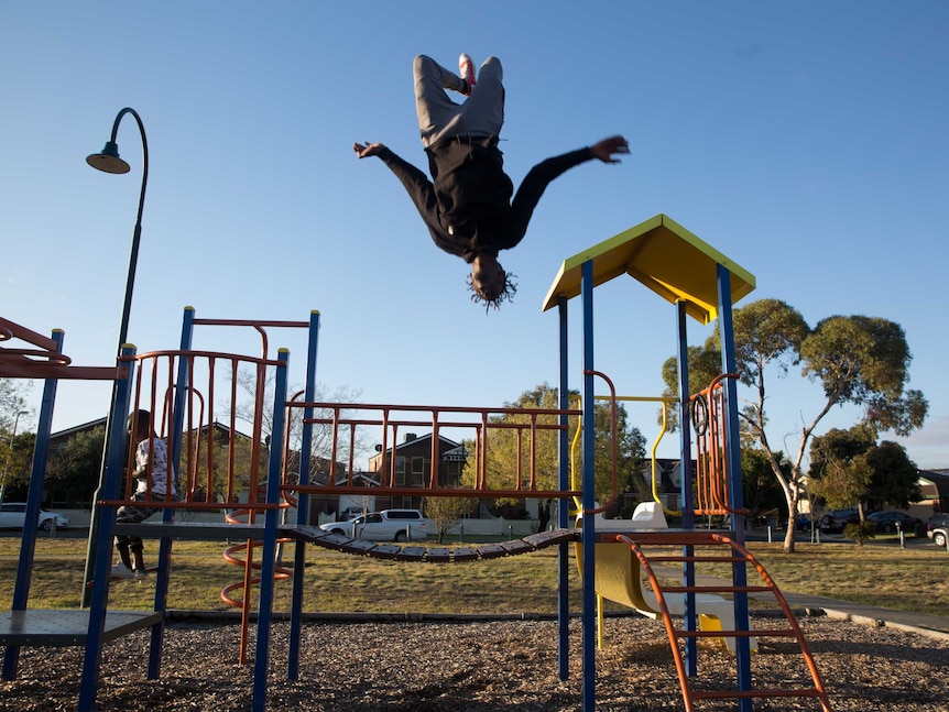 Mohamed's friend does a backflip off the suburban play ground.