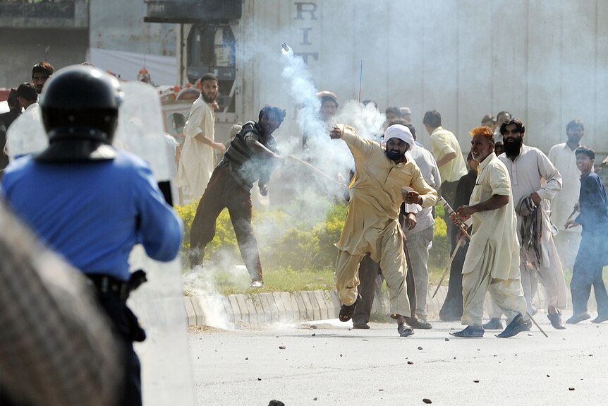 A Pakistani demonstrator throws a tear gas shell towards riot police