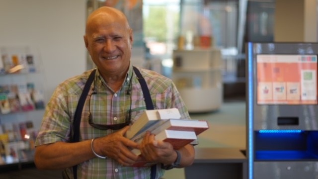 A man has a big smile as he holds a pile of books at Success Library.