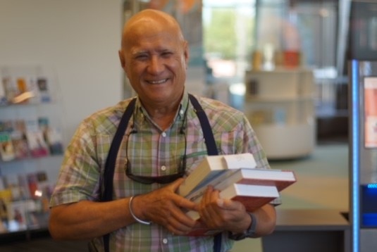 A man has a big smile as he holds a pile of books at Success Library.