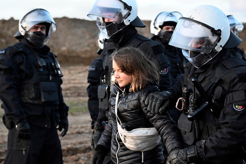 Greta Thunberg walking surrounded by riot police in helmets