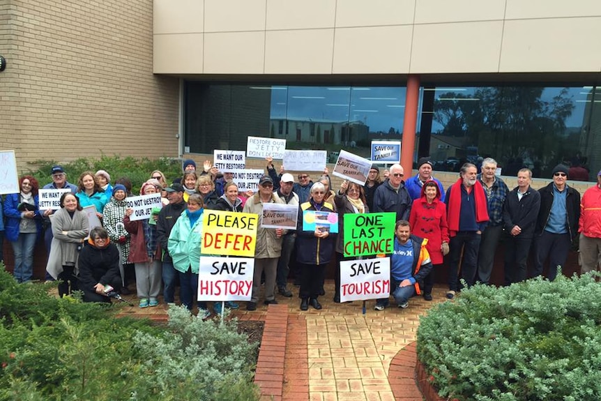 Image of a crowd of people with placards standing outside an office building.