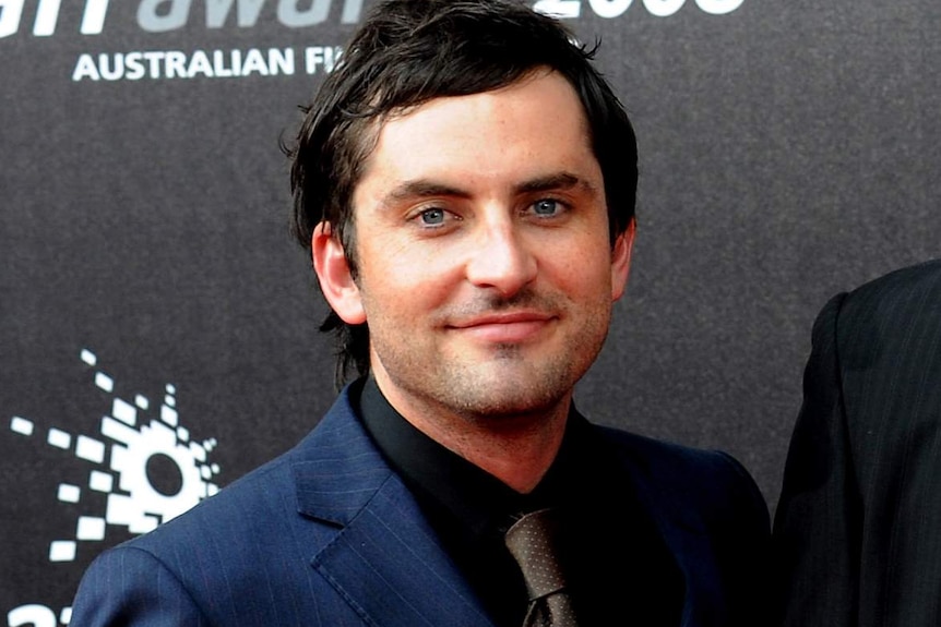 A smiling Daniel Houghton poses for a photo on the red carpet at the 2008 AFI awards in a blue suit and black shirt.