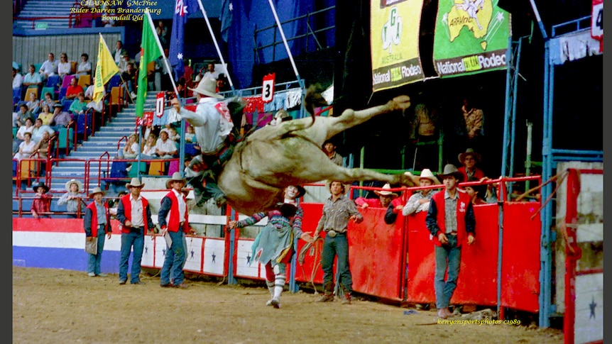 A bull leaps in the air while a rider clings to its back as stunned spectators watch on.