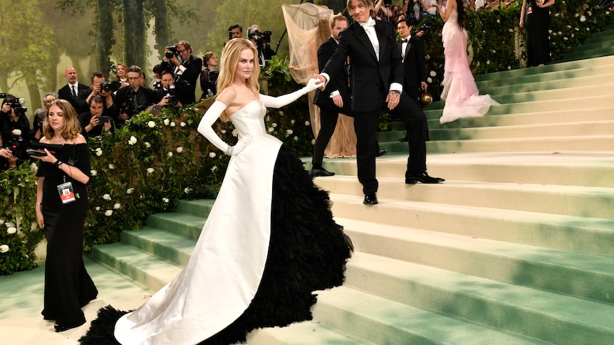 Nicole Kidman wearing a long silky white gown with black ruffly skirt and white sleeves. Keith Urban wears a black suit.