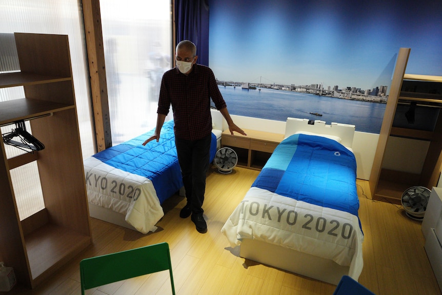 A journalist looks at cardboard single beds for the Tokyo 2020 Olympics with blue bedspreads with "Tokyo 2020" written on them