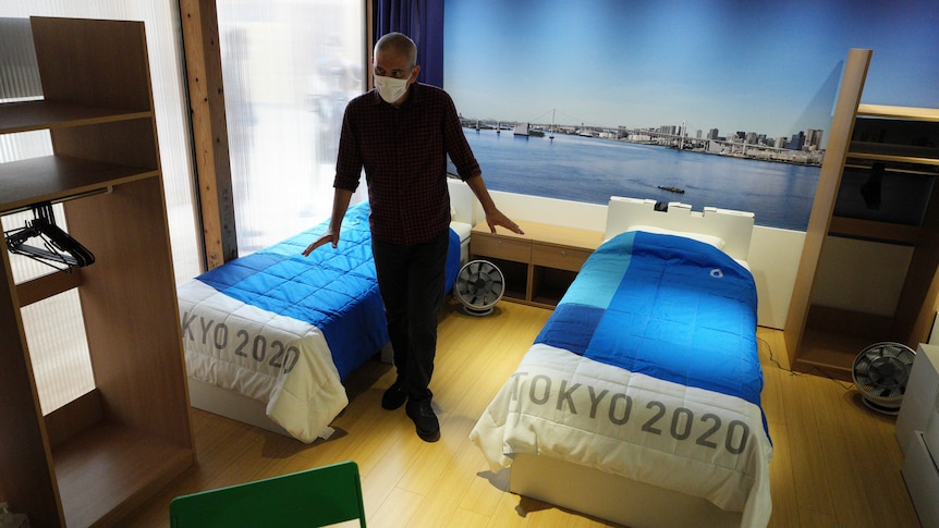 A journalist looks at cardboard single beds for the Tokyo 2020 Olympics with blue bedspreads with "Tokyo 2020" written on them