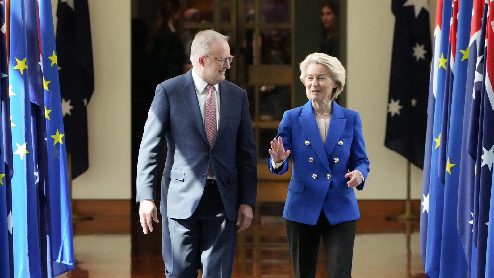 A man and a women in suits walk down a corridor lined in Australian flags.