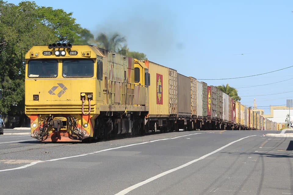 A train travels along a street in the middle of the road.